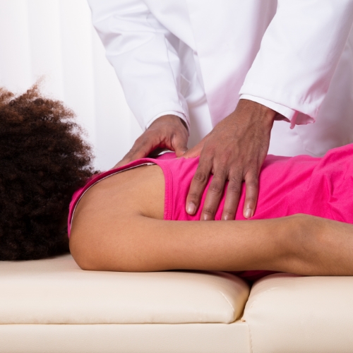 Female patient lying face down on massage table receiving manual therapy from a physical therapist on her upper back indicating back pain issues.